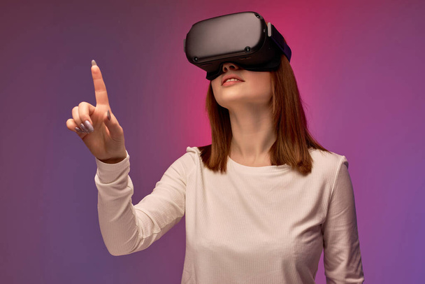 joyful young woman in virtual reality helmet, looking into VR glasses screen - Photo, Image