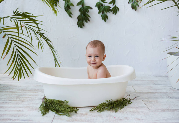 мальчик сидит в белой ванне на белом фоне с растениями. Копия пространства - Фото, изображение