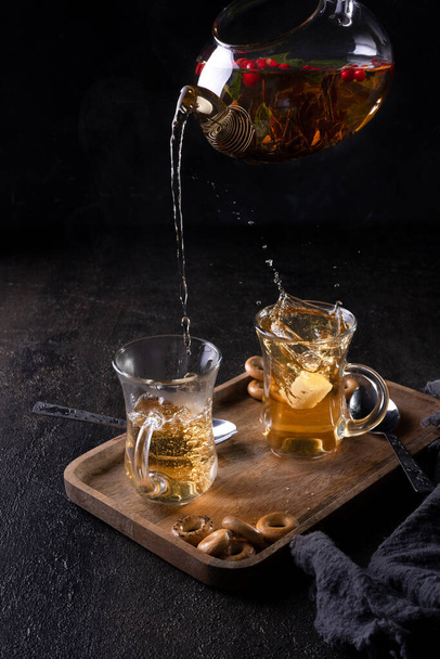 Pour black tea from a transparent teapot into a cup on black backround - 写真・画像