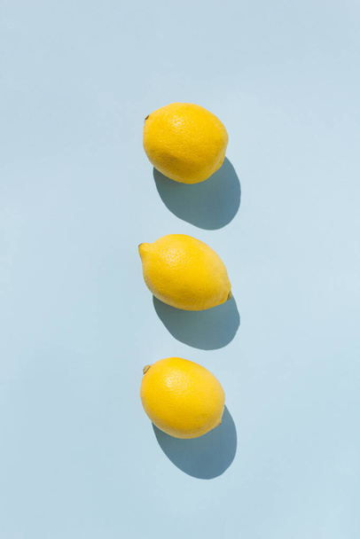 Neat composition of sunlit fresh lemons on pastel blue background. Trendy summer flat lay. Minimal healthy food concept. - Photo, Image