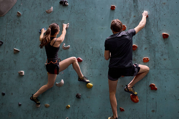 Active sporty woman and man practicing rock climbing on artificial rock - Foto, Imagen