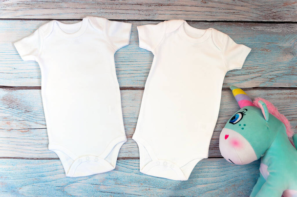 Layout Flat Put on a two white baby bodysuit on a wooden background with unicorn toy. Layout for design and placement of logos, advertising. Styled stock photography, stock photo. flat lay. - Photo, Image