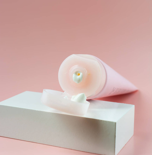 tubo rosa aperto con crema su un cubo bianco, sfondo rosa. copia spazio. - Foto, immagini