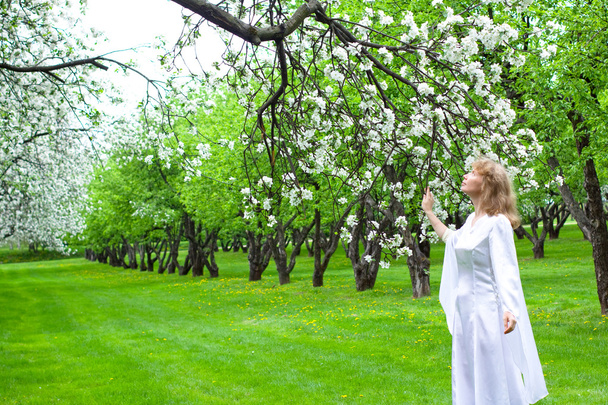 Tne blonde girl in white dress and apple-tree with white flowers - Fotó, kép