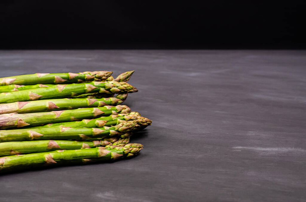 Stems of fresh green asparagus on a black background. Seasonal spring harvest. Flat lay, copy space. Healthy food concept. Close-up - Photo, image
