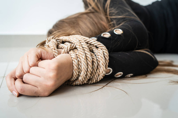 Close up on hands of Unknown caucasian woman or minor girl lying unconsciousness on the floor with rope tied arms - Human rights kidnapping trafficking violence concept selective focus - Photo, Image