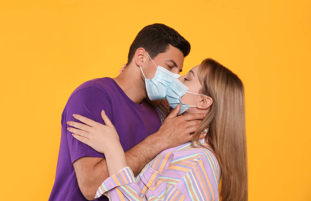 Couple in medical masks trying to kiss on yellow background - Foto, immagini
