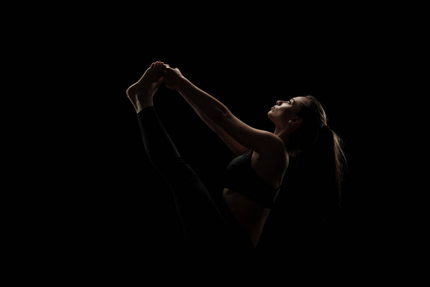 cute caucasian girl exercising yoga poses against dark backgroung. side lit silhouette. - Photo, Image