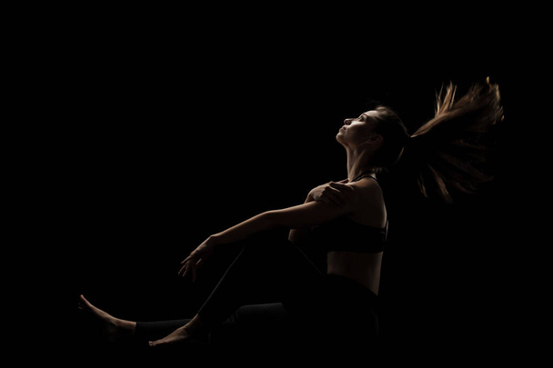 cute caucasian girl sitting with her hair in the air against dark backgroung. side lit silhouette. - 写真・画像