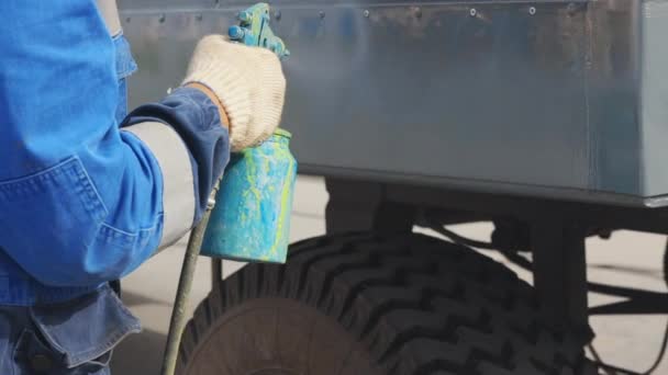 Automalyar paints large equipment from a spray gun. A worker wearing works outside on a summer day - Video
