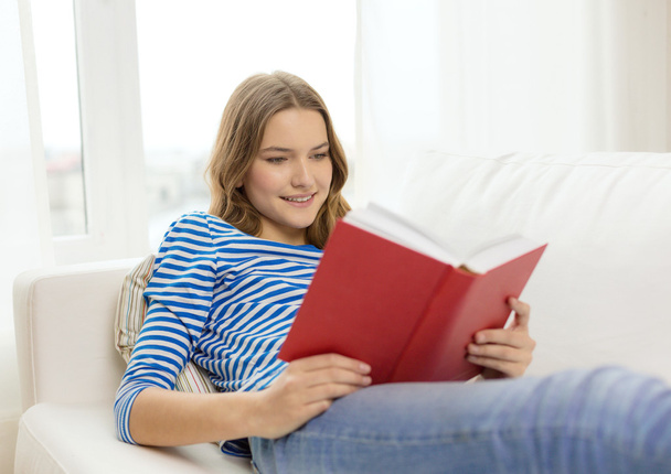 smiling teenage girl reading book on couch - Foto, imagen