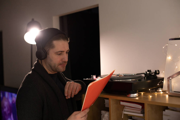 αξύριστος όμορφος hipster τύπος κοιτάζει κόκκινο φάκελο ρεκόρ ακούγοντας μουσική - Φωτογραφία, εικόνα
