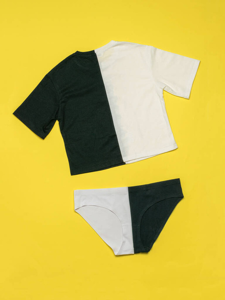 Conjunto de camiseta en blanco y negro y pantalones cortos en blanco y negro sobre fondo amarillo. Conjunto de ropa de verano en contraste. Puesta plana. - Foto, imagen