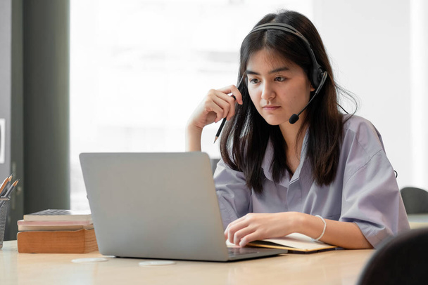 koncentrált fiatal ázsiai lány vagy diák nézi laptop gazdaság könyv tanulás, komoly nő dolgozik vagy tanul a számítógép csinál kutatás vagy felkészülés vizsgára online. - Fotó, kép