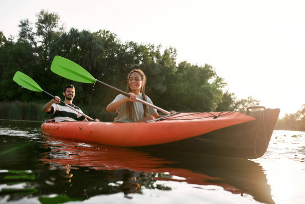 Smiling young woman and her boyfriend enjoying kayaking in a lake on a late summer afternoon - Foto, afbeelding