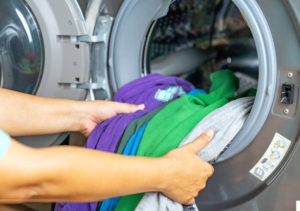 Μια γυναίκα φορτώνει χρώμα ρούχων πλυντήριο ρούχων στο σπίτι της. - Φωτογραφία, εικόνα