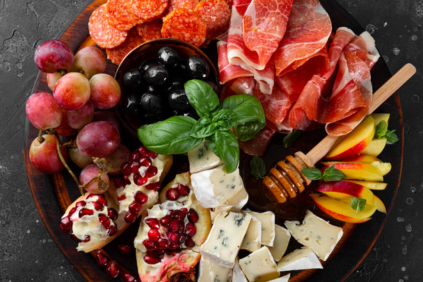  A set of appetizers for wine, jamon, pepperoni, cheese, grapes, peach and olives on a wooden board top view. Snack board close up - Фото, изображение
