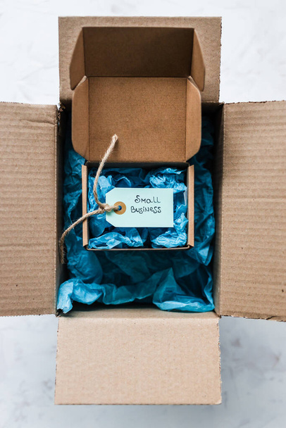 product tag with small business text inside ofsmaller delivery parcel inside of a bigger parcel, concept of customer behaviour and supporting small local businesses - 写真・画像