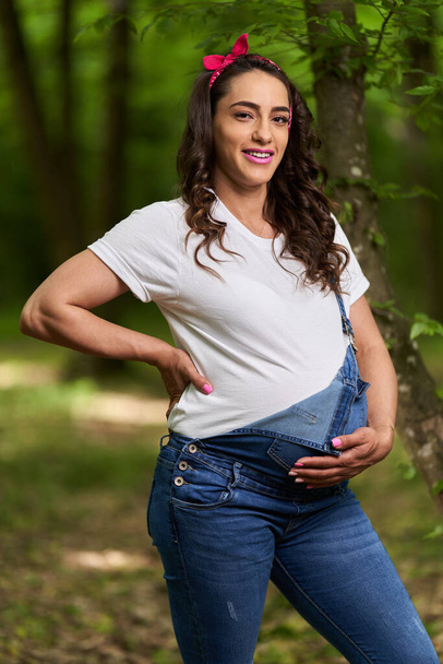 Portrait of a beautiful young hispanic pregnant woman in a deciduous forest in the summer - Photo, Image