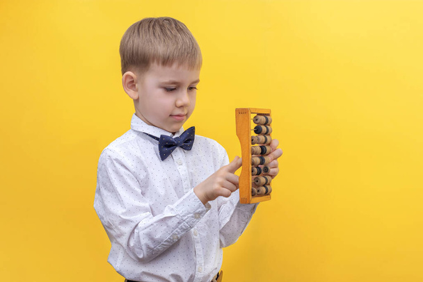 Cute blonde boy in a shirt holding a wooden abacus. The concept of the knowledge day, back to school  - Foto, Imagem