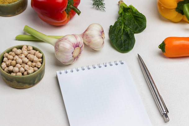 Pen and notebook. Bulgur in bowl. Garlic, pepper and spinach leaves on table. White background. Top view - Foto, imagen