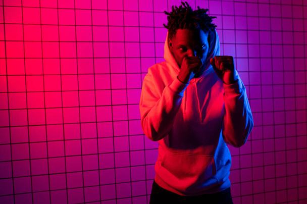 Portrait of an African American man in a hoodie on a neon background. Red-blue background. - Foto, afbeelding