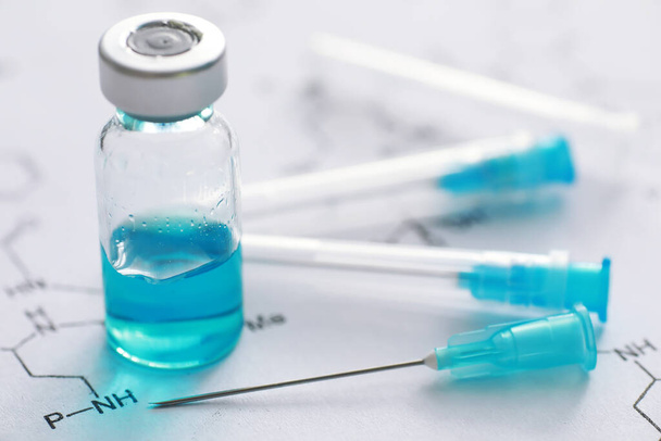 kleine Gläser mit Injektion und Spritze zur Injektion auf blauem Hintergrund in der Nähe der chemischen Rezeptur - Foto, Bild