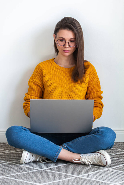 Young woman using laptop sitting on the carpet on white background - Fotografie, Obrázek