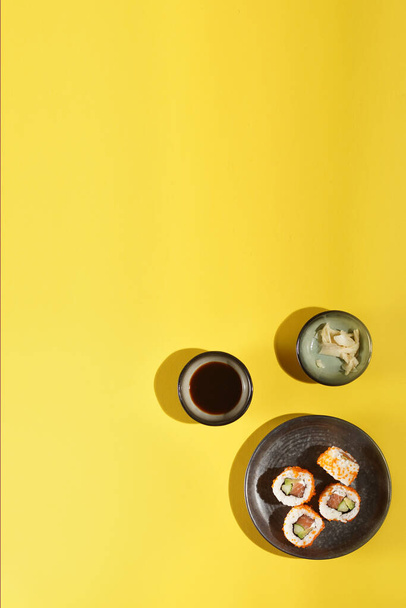 Sushi nigiri s lososem na černém talíři na žlutém pozadí, se sójovou omáčkou a zázvorem, výhled shora, šablona - Fotografie, Obrázek