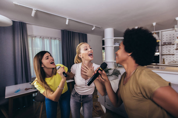 Young womanl singing into microphone at home party having fun. Bachelorette party, karaoke, music concert and holidays concept  - Foto, Imagen