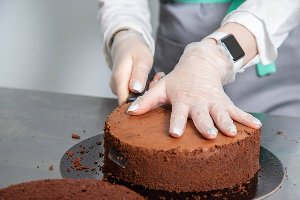 Womans hands chef cutting chocolate cake layers and stacking them on metal table. Making Chocolate Layer Cake. Series. - Foto, immagini