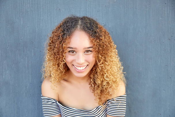 Lächelndes Porträt eines lateinamerikanischen Teenagers auf grauem Hintergrund. Nahaufnahme eines jungen Mädchens mit glücklichen lockigen Haaren.  - Foto, Bild