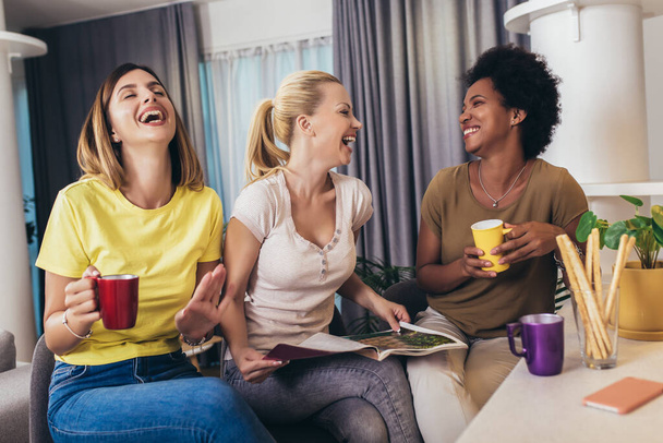 Τρεις νεαρές όμορφες χαμογελαστές γυναίκες διαβάζουν περιοδικά στο σπίτι. - Φωτογραφία, εικόνα