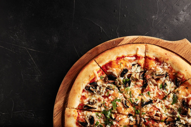 pizza na drewnianej podstawie na czarnym teksturowanym tle widok z góry - Zdjęcie, obraz