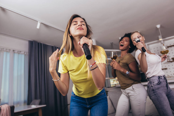 Young womanl singing into microphone at home party having fun. Bachelorette party, karaoke, music concert and holidays concept  - 写真・画像