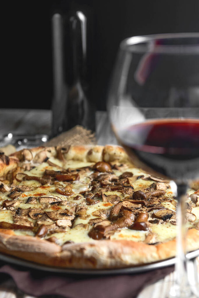 Appetizing pizza with mushrooms on a rustic wooden background. Delicious vegetarian pizza. Traditional recipe, Italian cuisine concept. Served with red wine. - Photo, Image