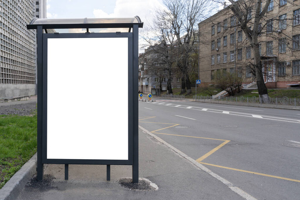 Svislý prázdný bílý billboard na autobusové zastávce na městské ulici. silnice a domy v pozadí. Vysmívej se. prázdný Reklamní billboard na ulici vedle silnice, denní záběr - Fotografie, Obrázek