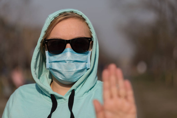 Concepto de Coronavirus Llamada global para quedarse en casa. Chica con máscara protectora de la enfermedad y mostrar gesto de manos de parada para detener el brote de coronavirus. - Foto, imagen
