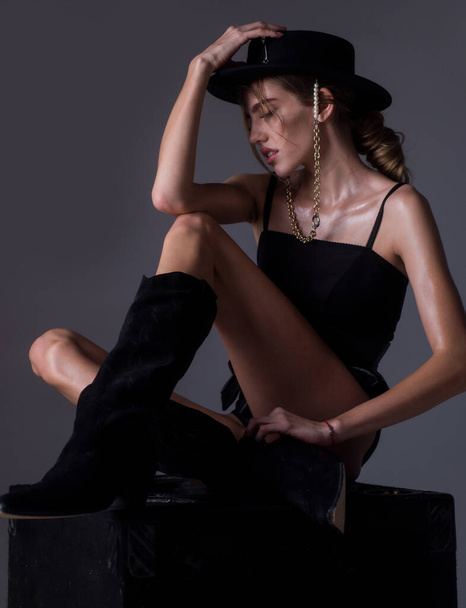 Beautiful sensual woman fashion model in trendy clothes wearing a black round hat. Sexy female posing in studio. Beautiful high fashion female model with beauty face. Fashion boutique advertising. - Фото, зображення