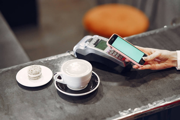 Dziewczyna płacąca za latte smartfonem za pomocą bezdotykowej technologii PAY PASS - Zdjęcie, obraz