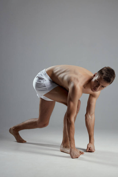 man doing sports indoors in white shorts leaning forward side view - Photo, Image