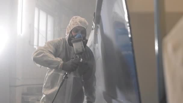 フードやマスクと白い保護スーツを着た男性労働者の中程度のショット,表面に青色の塗料を噴霧 - 映像、動画