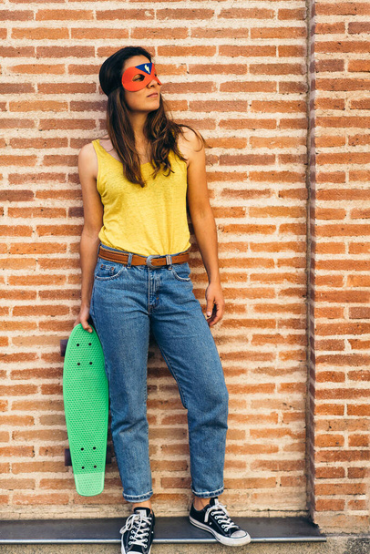Cool σούπερ ήρωας γυναίκα θέτει με skateboard. - Φωτογραφία, εικόνα