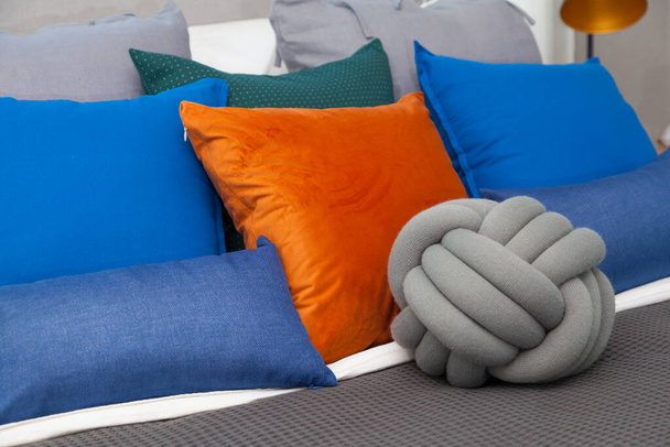 Oreiller bleu et orange sur lit king size dans une chambre contemporaine avec lampe moderne et vase sur table de chevet. - Photo, image
