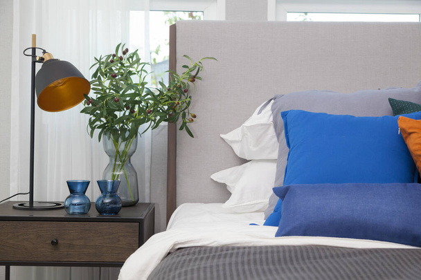 Blue and orange pillow on king size bed in contemporary bedroom with modern lamp  and vase on nightstand table. - Fotoğraf, Görsel