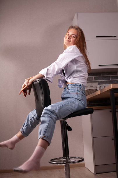Portrait of a beautiful blonde girl in simple everyday things sitting indoors. - Fotó, kép