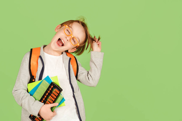 Веселий школяр на зеленому тлі. Щаслива дитина в окулярах з рюкзаком і блокнотами. Повернутися до школи та освіти. Шкільна дитина на уроках. Початкова школа
. - Фото, зображення
