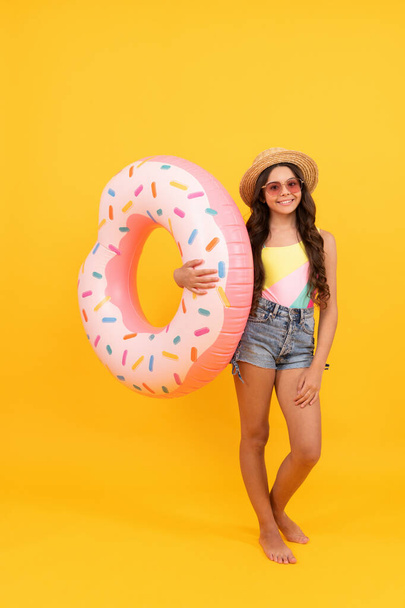 happy beach kid with curly hair in straw hat and sunglasses with doughnut inflatable ring for pool party fun on summer vacation on yellow background, summer vacation. - Foto, afbeelding