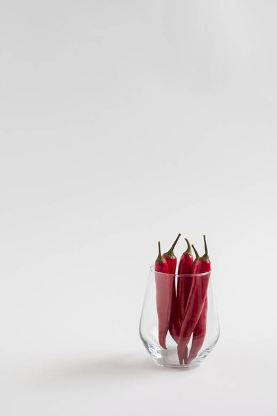Red chili peppeprs in a transparent glass stand on a white background, vertical composition with copy space - Photo, Image