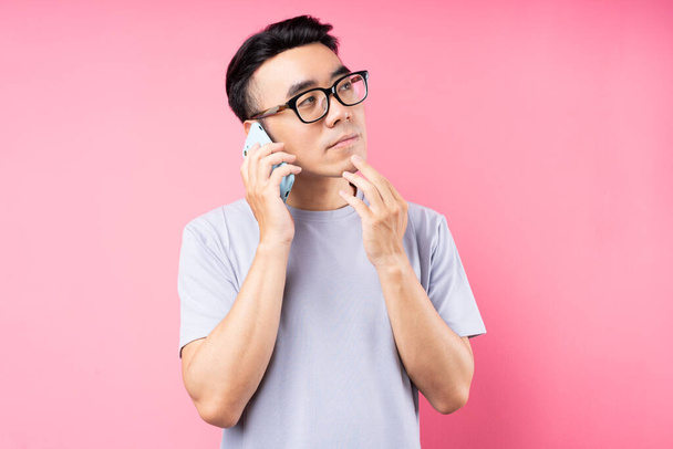 Portrait of Asian man using smartphone on pink background - Photo, Image